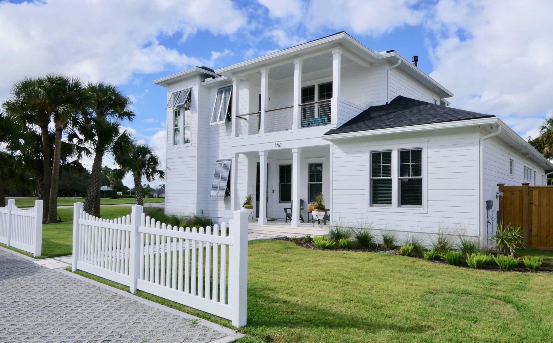 White two-story house with a porch and white picket fence under a blue sky.