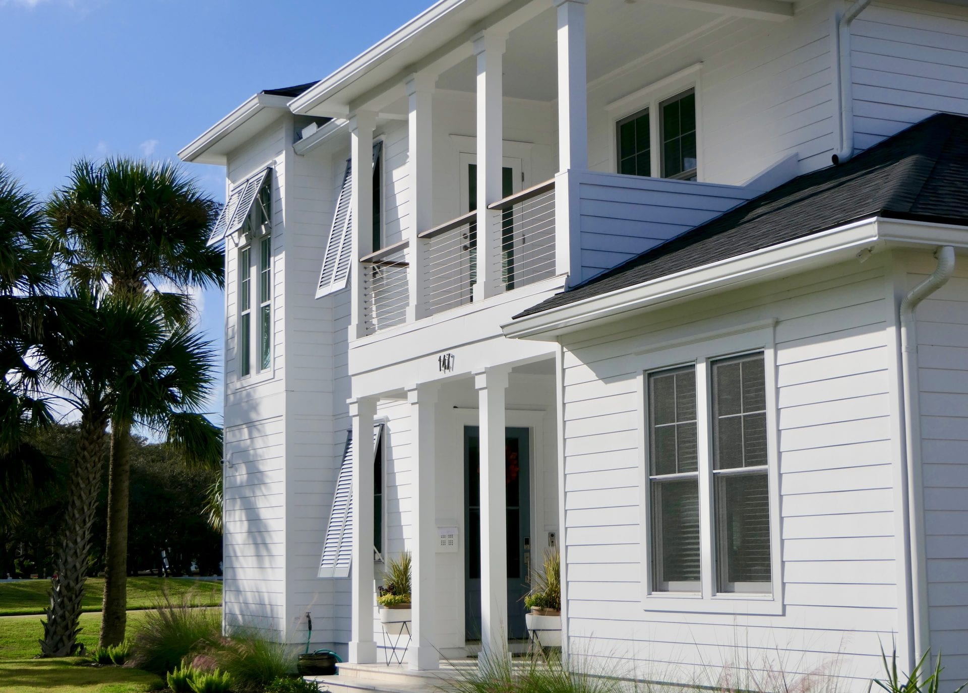 White two-story house with balconies and columns under a clear sky.