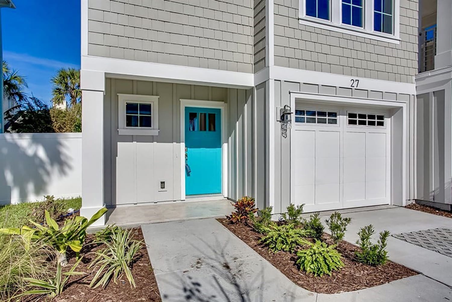 Modern house entrance with a bright turquoise door and neat landscaping.