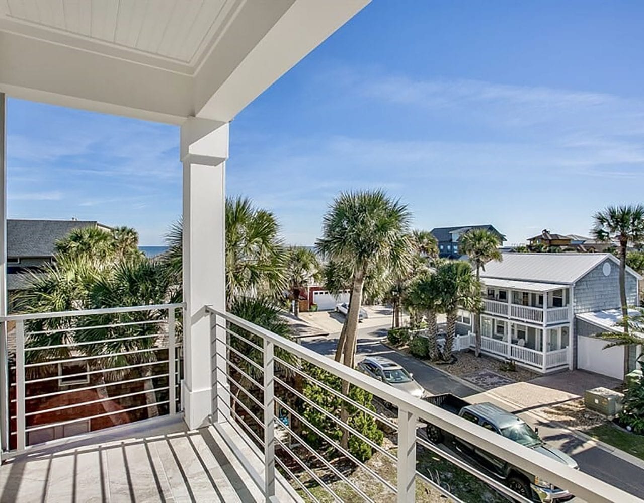 Balcony view overlooking a sunny neighborhood with palm trees and houses.