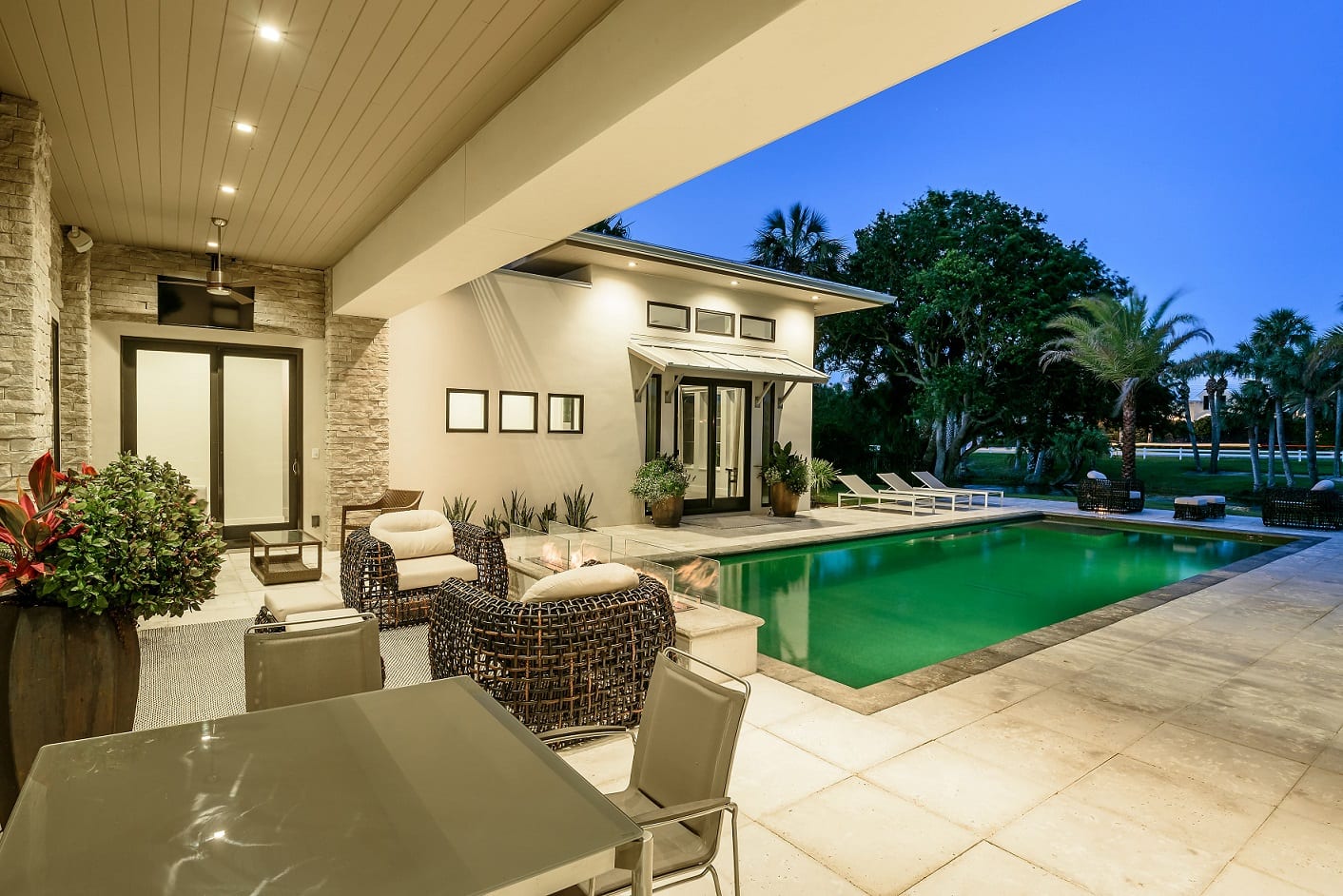 Modern outdoor patio with seating and a lit swimming pool at dusk.