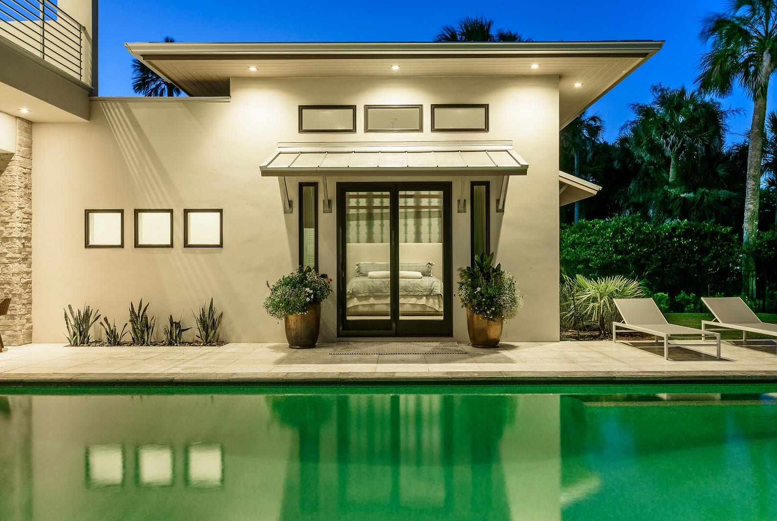 Modern pool house with glass doors and warm lighting at dusk.