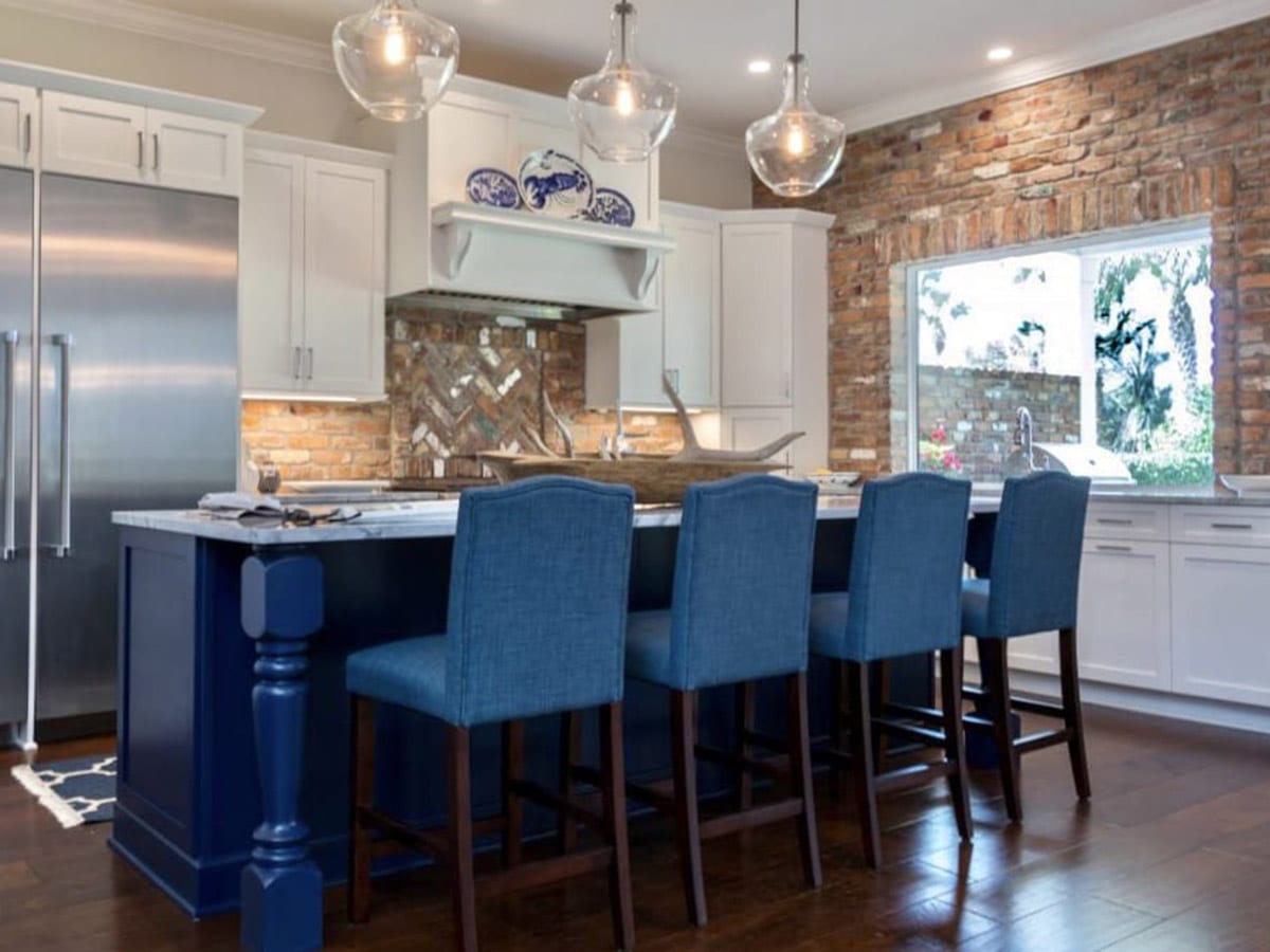 Modern kitchen with blue bar stools and exposed brick wall.