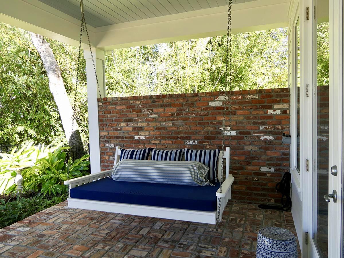 A cozy porch swing with striped cushions and a brick wall backdrop.