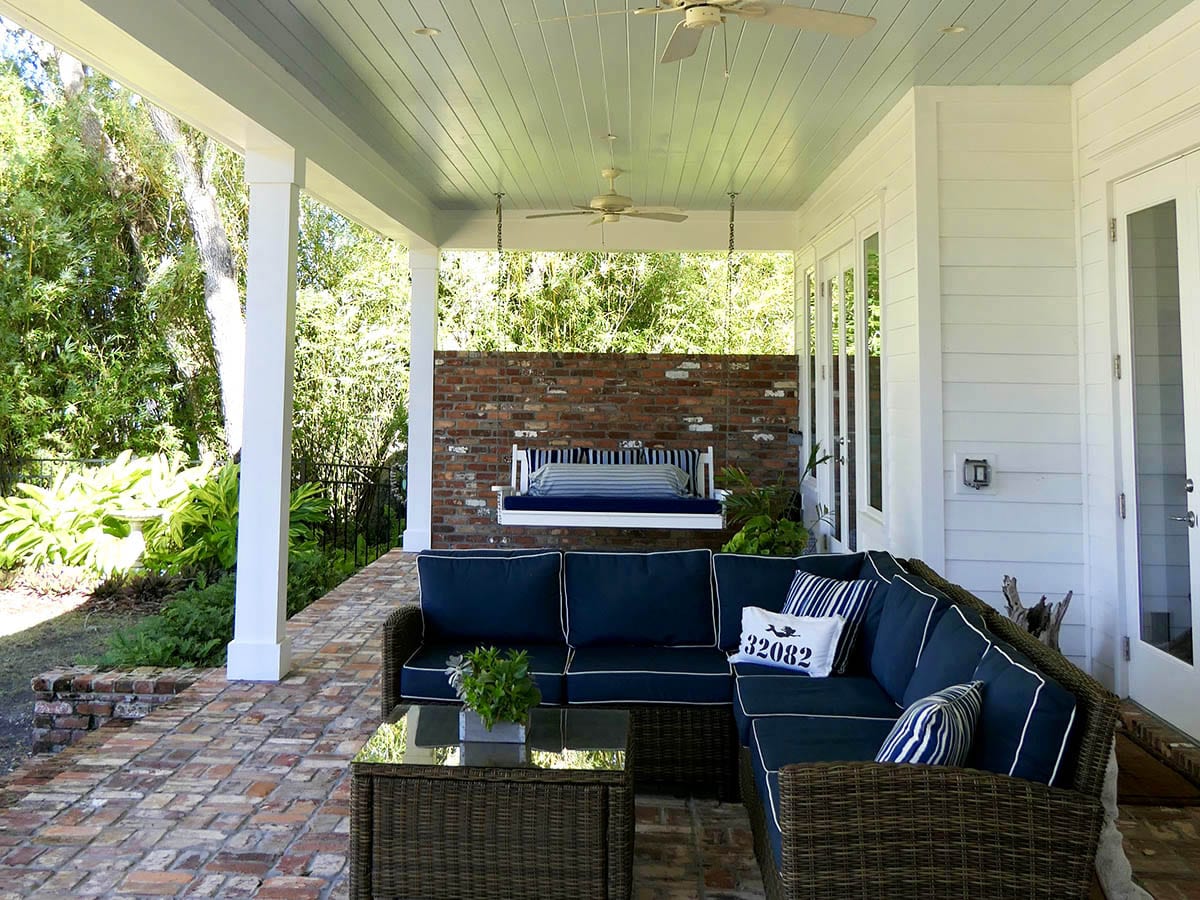 Cozy covered porch with navy blue wicker furniture and a hanging swing bed.