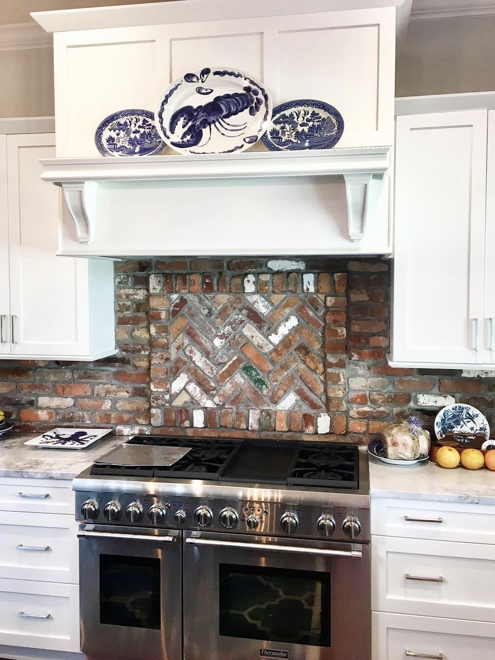 Modern stove with rustic brick backsplash and white cabinetry in kitchen.