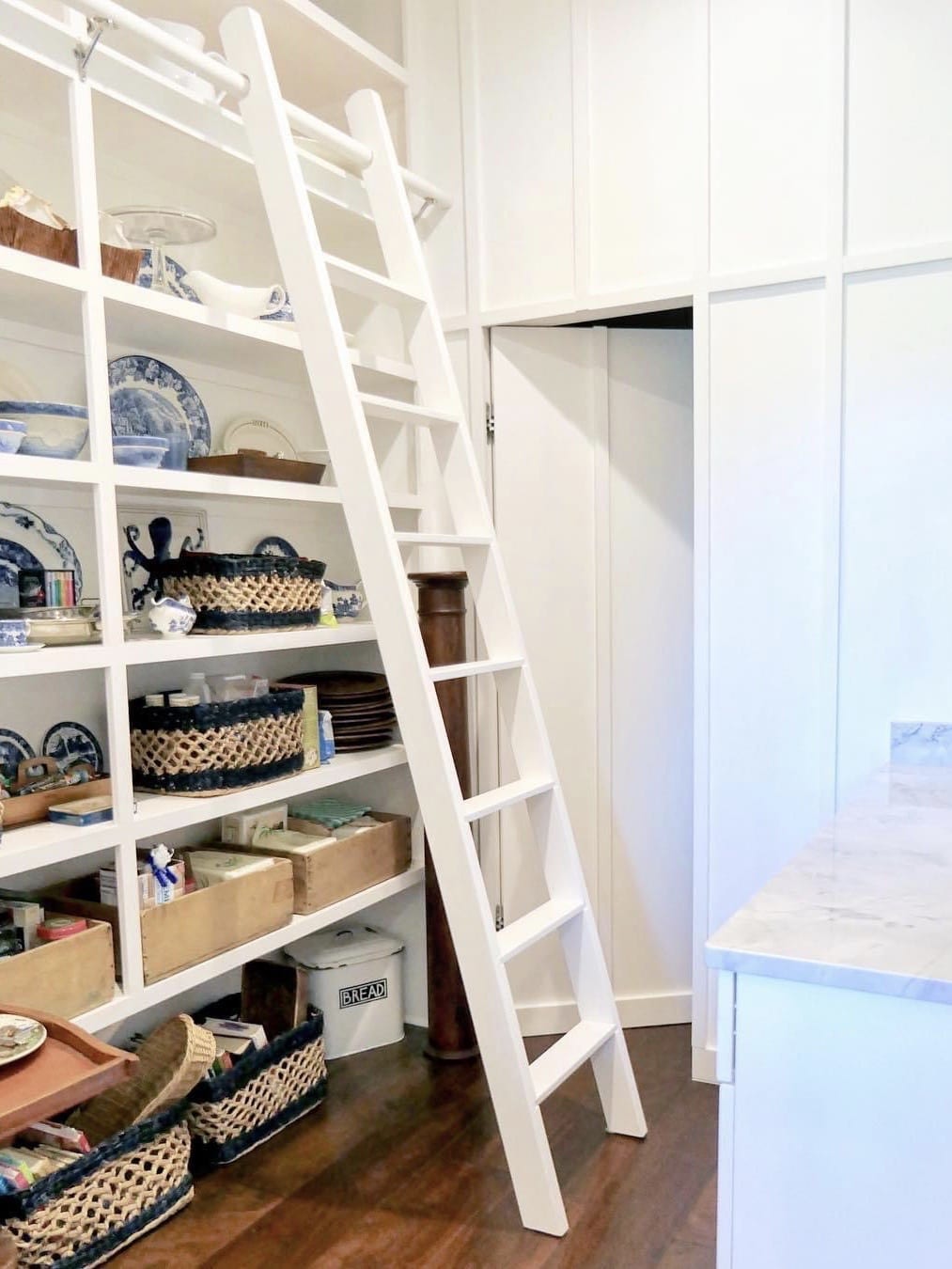 White pantry shelves with a ladder and woven baskets for storage.