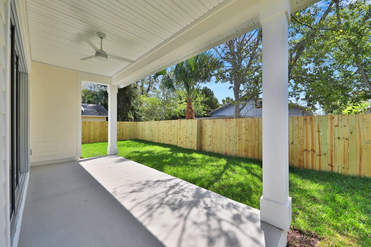 Sunny backyard patio with green lawn and wooden fence under a covered porch.