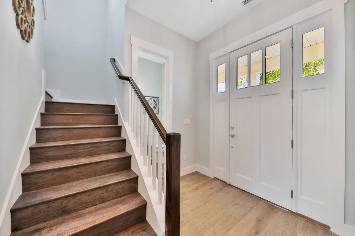 Bright entryway with wooden stairs and white door.