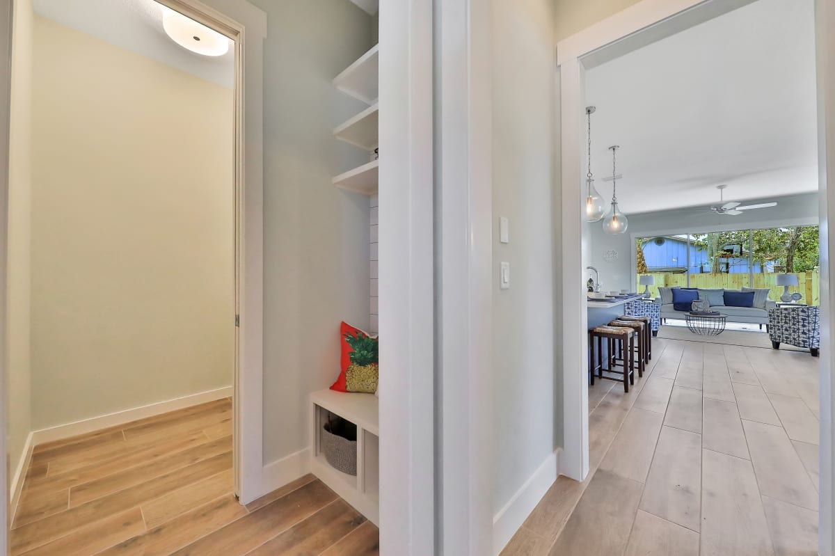 A narrow pantry with shelves and storage space beside a bright kitchen.