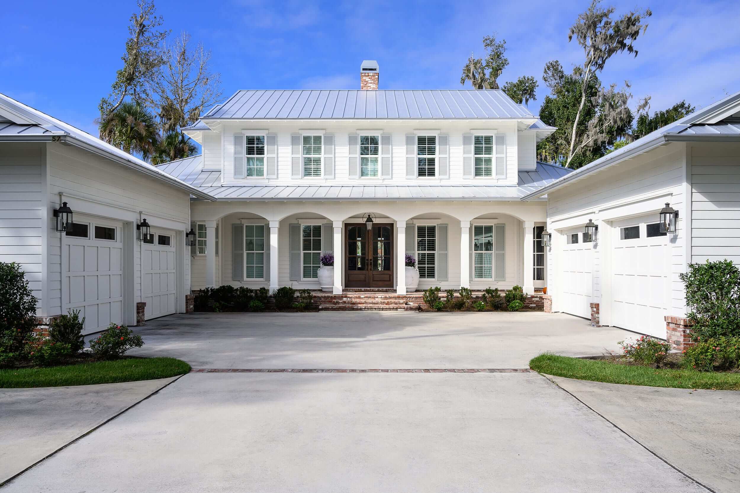 Elegant two-story white house with a metal roof and symmetrical design.