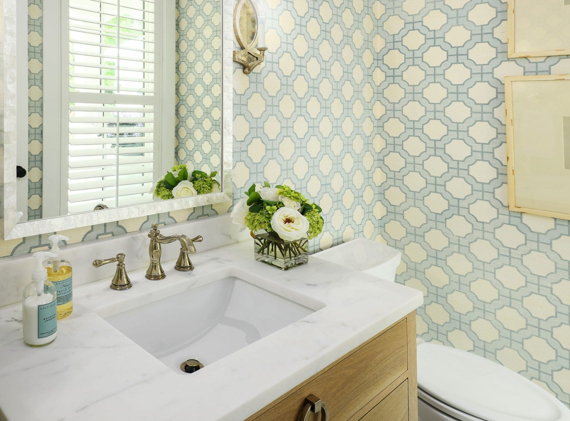 Elegant bathroom sink area with patterned wallpaper and fresh flowers.