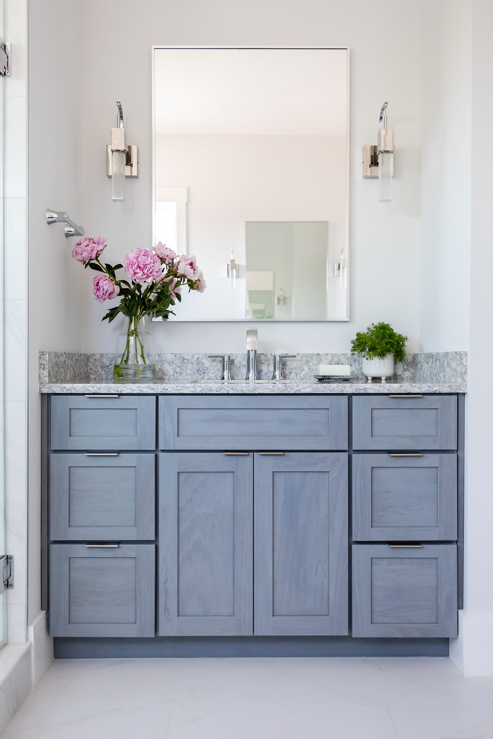 Elegant bathroom vanity with blue cabinets and pink flowers on granite countertop.